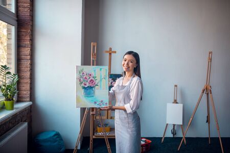 Real talent. Nice talented woman standing in the studio while showing you a flower paintingの写真素材