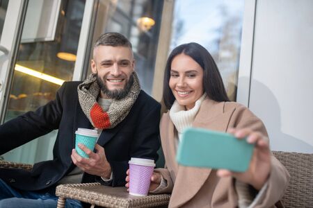 Taking photos. Positive delighted woman holding her smartphone while taking a selfie during breakfastの写真素材