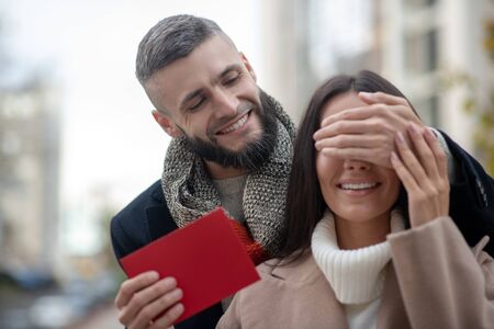 Do not look. Nice young man covering his girlfriends eyes while having a surprise for herの写真素材