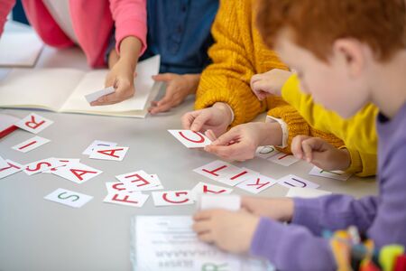 Learning letters. Close up picture of a school desk with different cards on it and children sitting aroundの写真素材
