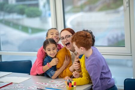 A favourite teacher. A group of schoolchildren hugging a smiling teacher
