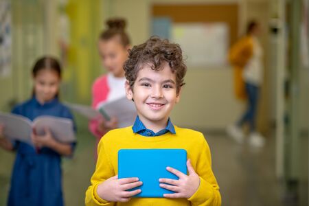 Cheerful mood. Smiling pupil standing in the school corridor in front of his classmates going to the lessonの写真素材