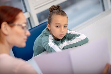 Sharing feelings. Upset schoolgirl leaning on the desk and looking at her caring teacherの写真素材