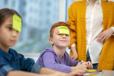 Pretending game. Smiling pupil wearing a sticker with word parrot on it during the lesson