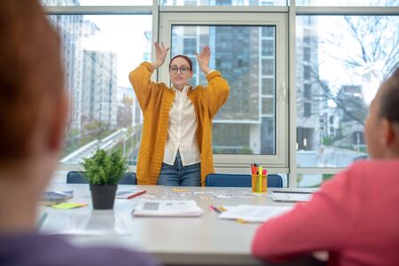 Funny teacher. Easy-going teacher showing her teacher meaning of the words standing in front of themの写真素材