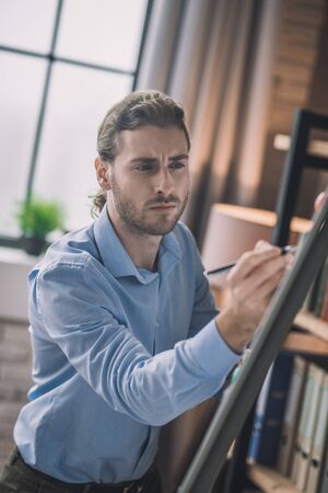 Making schemes. Young bearded man in eyeglasses writing on white boardの写真素材