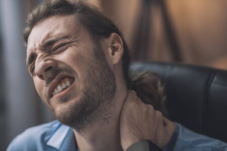 Painful feeling. Young bearded man in blue shirt suffering from aching neckの写真素材