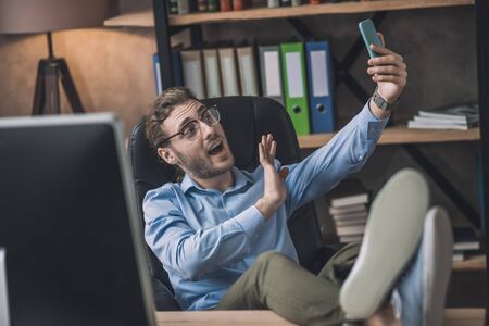 Good mood. Young bearded office worker in eyeglasses making selfie