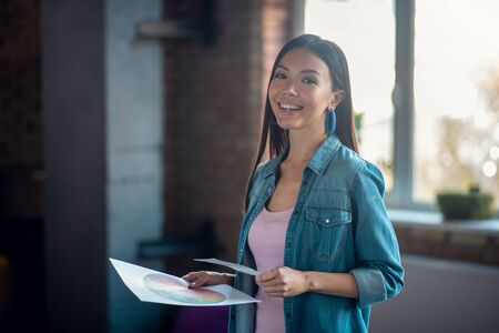 In the office. Happy Asian woman smiling while standing against the window in her office.