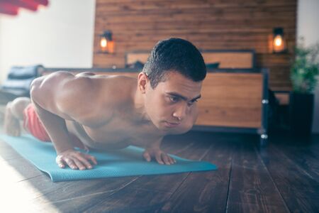 Push ups. Handsome dark-haired man in red shorts doing push ups