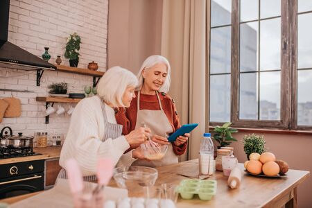Surfing internet. Grey-haired smiling ladies in aprons looking involvedの写真素材