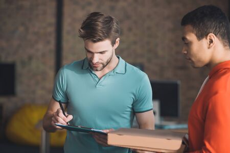 Where to sign. Handsome bearded man looking at the invoice while checking where to sign it