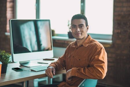 At my workplace. Nice smart man turning to you while sitting in front of the big monitorの写真素材