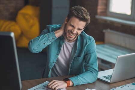 I feel pain. Good looking young man touching his neck while suffering from painの写真素材