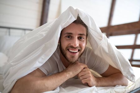 Nice morning. Young bearded man having fun in bed in the morningの写真素材
