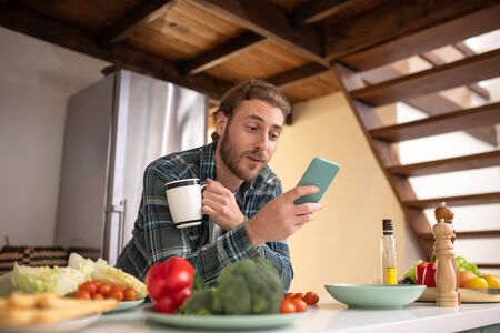 Multitasking. A surprised man texting drinnking tea and cooking simultaneuoslyの写真素材