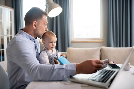 Father and a daughter. Man in a blue shirt working and holding his daughterの写真素材