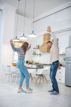 Dancing time. Cheerful and carefree father with daughter dancing at home in the kitchen.の写真素材