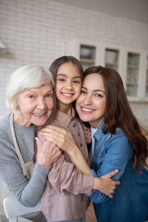 Womans happiness. Three beautiful women daughter mom and grandmother hugged together in the kitchen,...