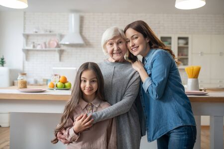 Relatives. Mom, daughter, grandmother standing in the kitchen together hugging, beautiful happy and...
