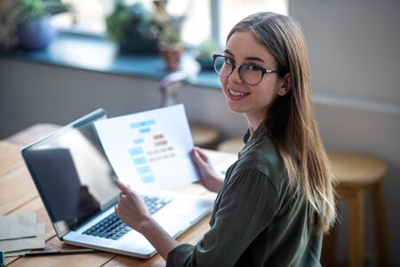 Analysis of the work done. Girl with glasses sitting at a table in front of a laptop holding a...