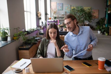 New idea for business. Young smiling man in glasses and with a project in hand pointing to a laptop screen and an interested girl discussing a new idea, looking at a laptop.の写真素材