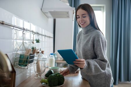 Pleased girl. Dark-haired girl in a grey sweater holding a tablet and smilingの写真素材