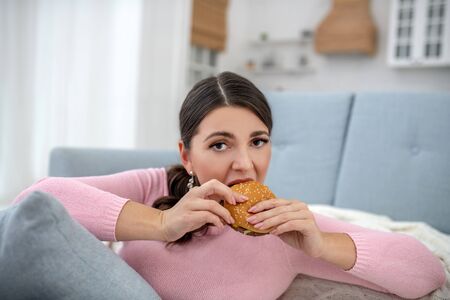 Burger. Full-figured young woman in a pink shirt eating a burgerの写真素材