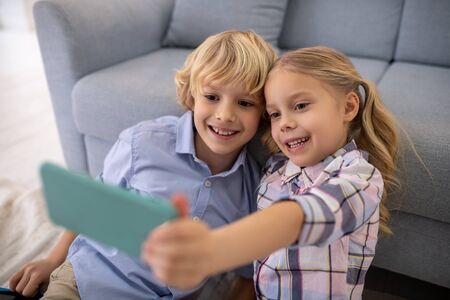 At home. Boy and girl sitting on the floor, taking selfie and smiling