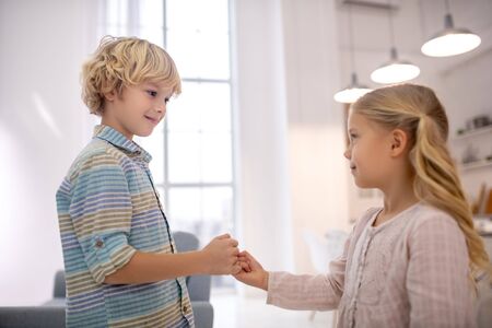 At home. Boy and girl clenching little fingers, looking at each other and smiling