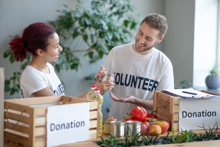 Packing food for needy. Young bearded man and girl with colored hair, standing at the table with...