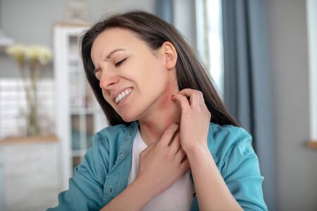 Eating habits. A woman itching her neck because of alergy