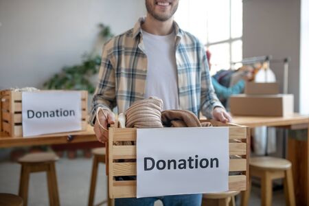 Humanitarian aid box. Wooden box with the inscription donation and with clothes, it is in the hands of a man in a plaid shirt.の写真素材