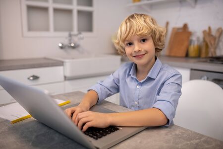 Positive mood. Cute blond boy typing on a laptop and smilingの写真素材