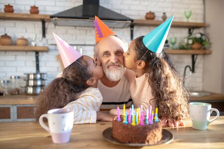 Love and happiness. Dark-skinned girls celebrating his granddads bithday and kissing him on cheeksの写真素材