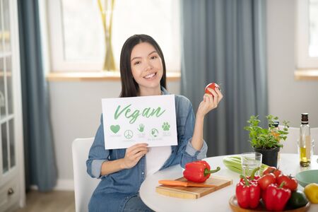 Only plant foods. Pretty young woman sitting with a poster and a red tomato in her hands, on the...