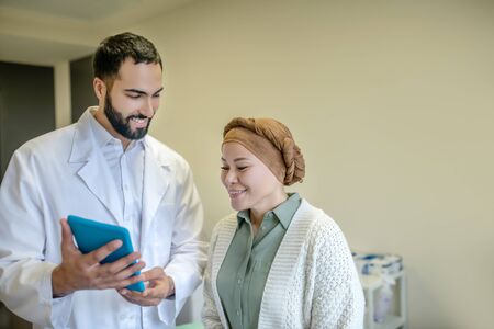 Information from internet. Bearded young doctor showing something on the tablet to his patient