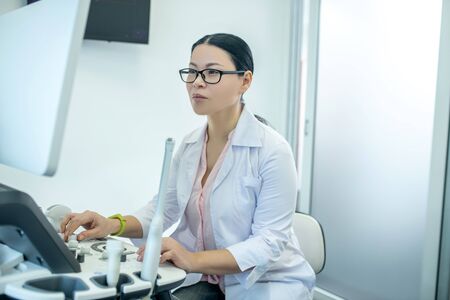 Busy at work. Female doctor in eyewear sitting at the ultrasonic device looking concentratedの写真素材