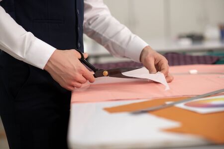 Fashion design studio. Hands of male tailor cutting out paper pattern