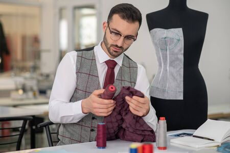 Fashion design studio. Male tailor holding dark scarlet cloth and spool, matching colors
