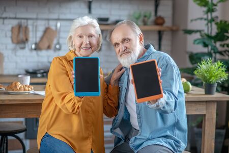 Easy to use and stylish gadgets. Elderly man and woman showing their tablets in colourful casesの写真素材