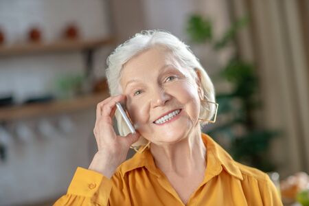 Making a phone call. A cheerful elderly woman talking on the phone with her friendの写真素材