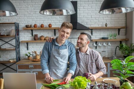 Beautiful day. Young gay couple making breakfast together and smilingの写真素材