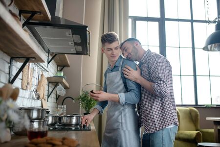 Male couple. Male couple standing near the hob engaged in cooking in the kitchen at home, caring happy.の写真素材