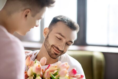 Expression of feelings. Two happy young men being close to each other and a bouquet of flowers, indoors.の写真素材