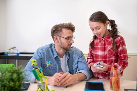 School classroom. Dark-haired girl holding control unit, discussing something with teacherの写真素材