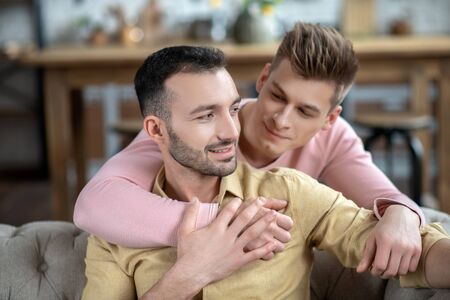 Hugs. Young fair-haired man putting hand on his partners shoulder