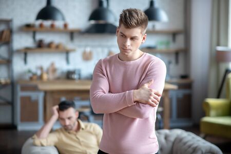 Bad mood. Man in pink shirt standing with his arms crossed after argument with his partnerの写真素材