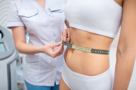 Nutrition specialist. Slim woman wearing underwear coming to nutrition specialist measuring her waistの写真素材