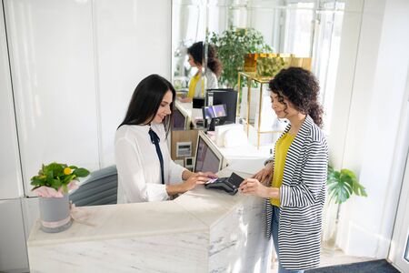 Payment in the store. Dark-haired female customer standing near cashier in the store ready to pay